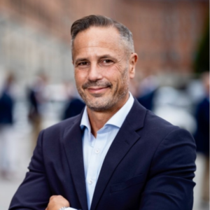 Profilbild på man i mörkblå kostym och brungrått hår.