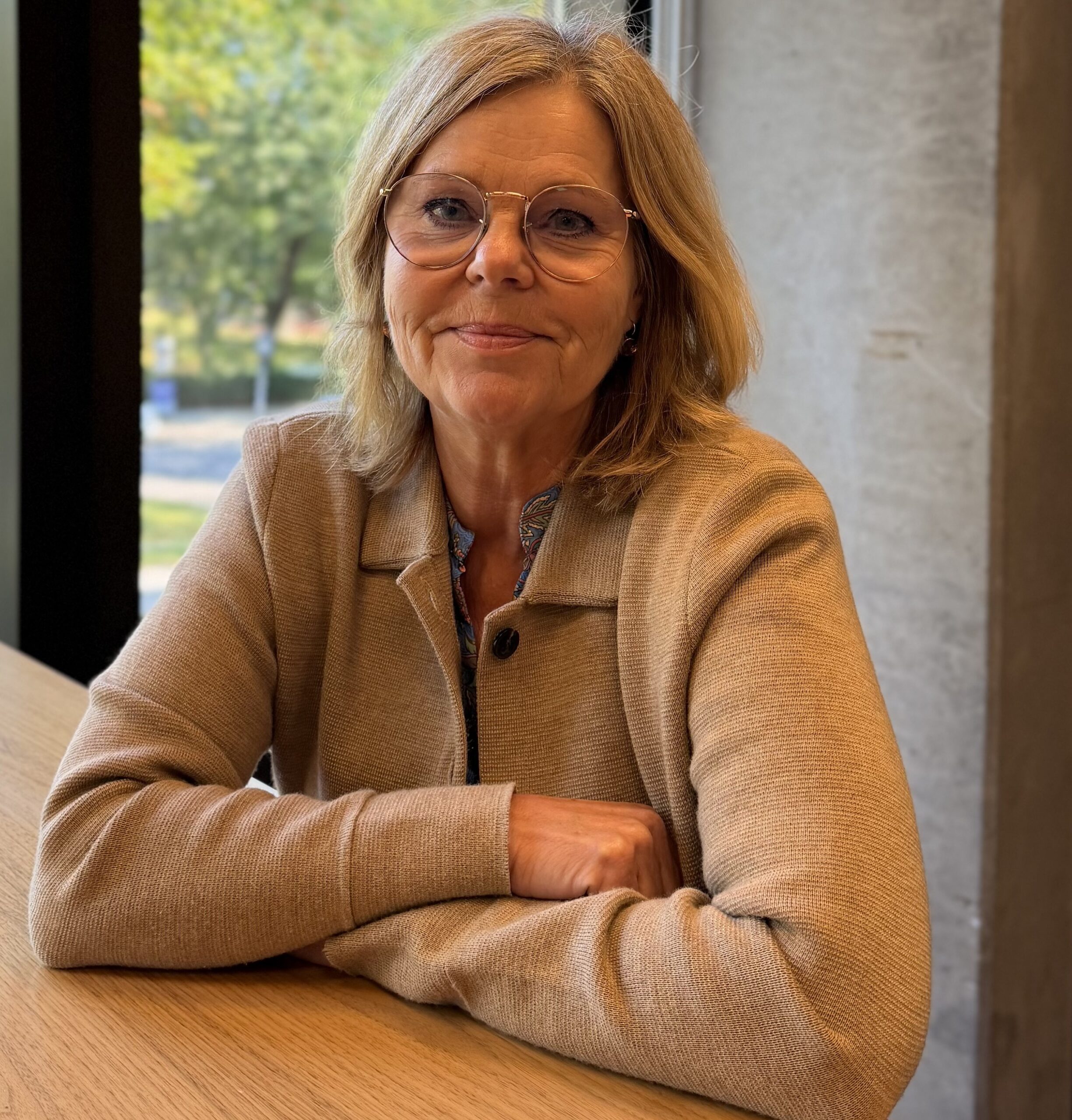 Porträtt på kvinna i blond page och glasögon och beige tröja